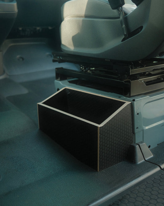 Black storage box in a vehicle's open cargo area with a seat in the background.